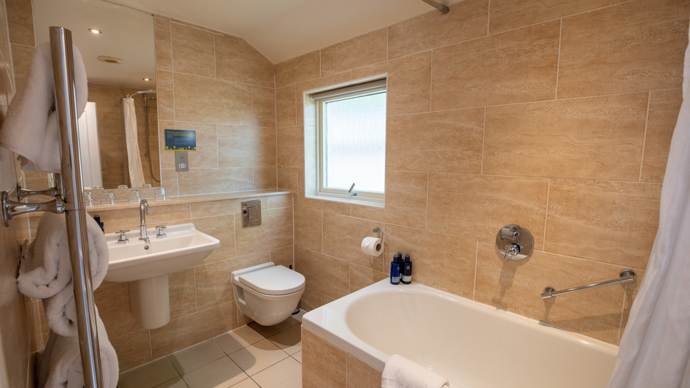 Bathroom in studio apartment with sink, toilet, mirror, shower over bath, and towel rack