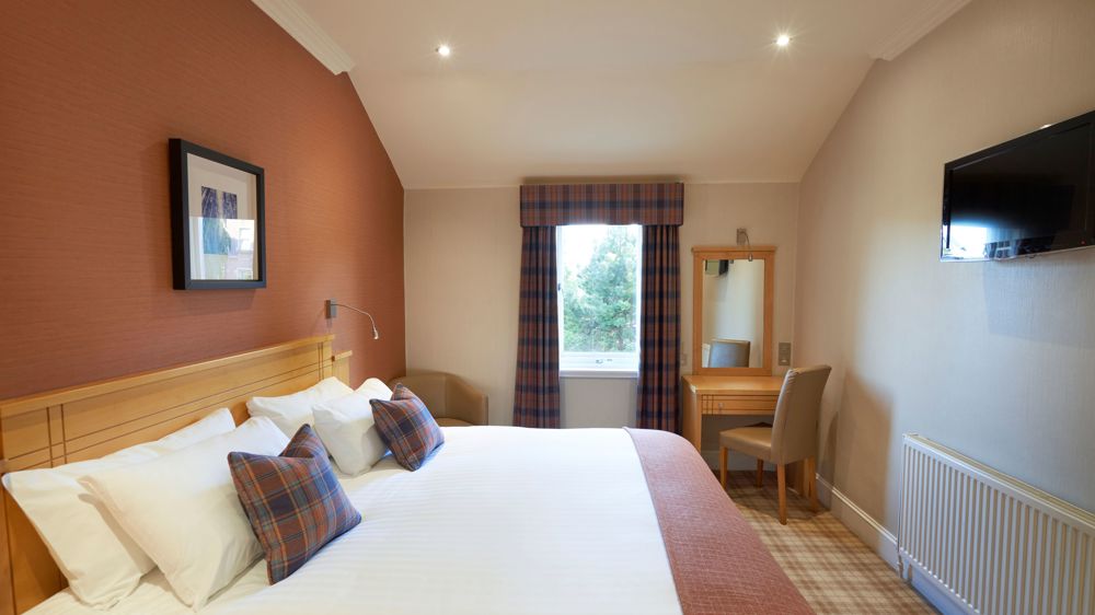 A room with double bed, a vanity, and a TV on the wall.