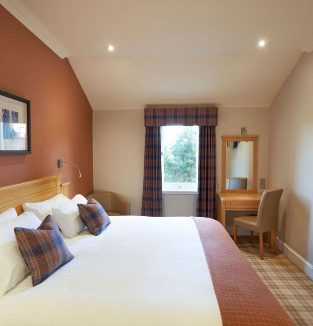 A room with double bed, a vanity, and a TV on the wall.