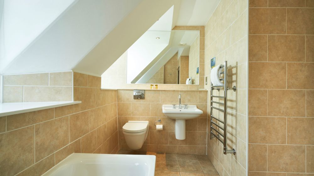 Bathroom with toilet, sink, towel rack, and bathtub. The ceilings are sloped.