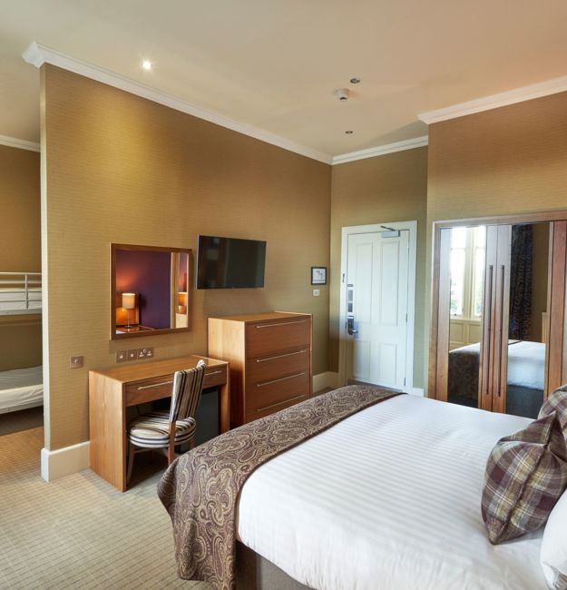 Room with king-sized bed, vanity, TV, dresser, and bunk beds partially behind a wall