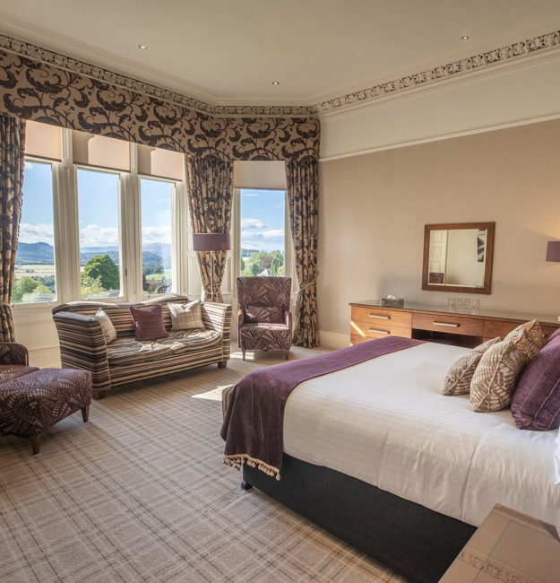 Leigh signature double with king-sized bed facing a window with two chairs and a loveseat in front of the window.