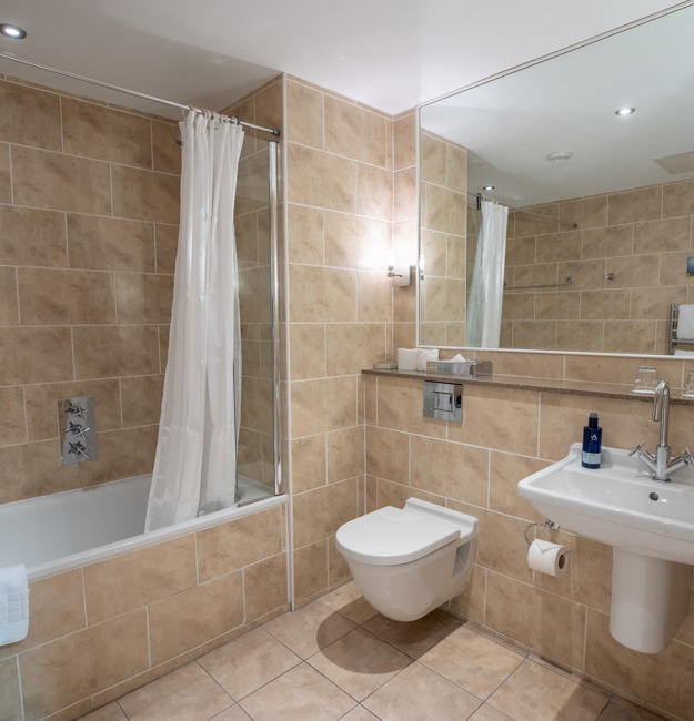 Bathroom with shower over tub, toilet, sink and mirror.