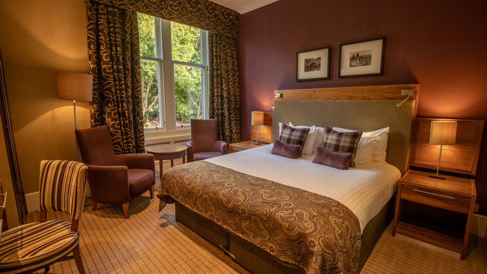 Feature double bedroom with king-sized bed, bedside table, two chairs in front of a window.