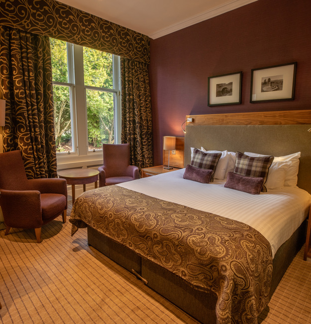 Feature double bedroom with king-sized bed, bedside table, two chairs in front of a window.