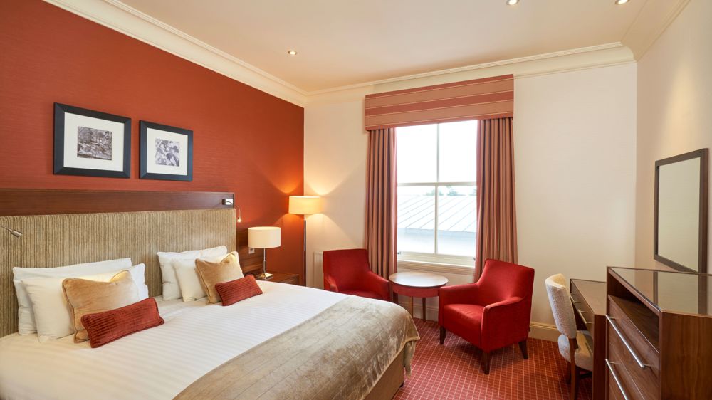 Feature double bedroom with king-sized bed, bedside table, two chairs in front of a window.